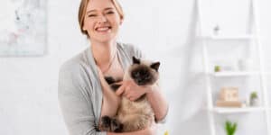 Siamese cat beinmg held by woman